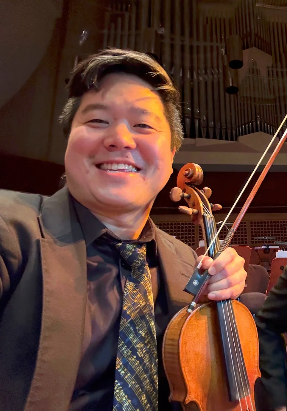 Leyan Lo smiling in concert attire while holding his violin and bow